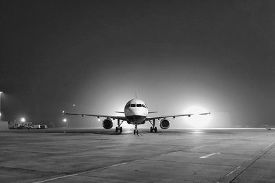 Airplane on airport runway against clear sky at night