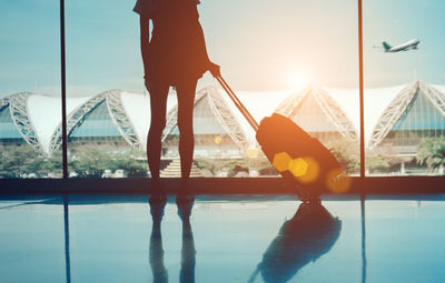 Low section of woman standing holding luggage at airport departure area