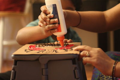 Cropped hands of mother and son making craft on table