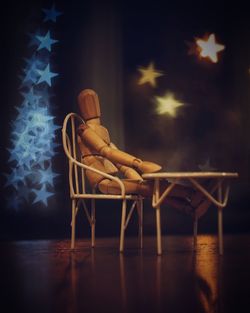 Wooden doll on small chair at table against christmas lights