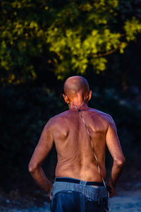 Rear view of shirtless man walking against tree