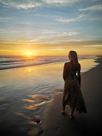 Rear view of woman standing at beach against sky during sunset