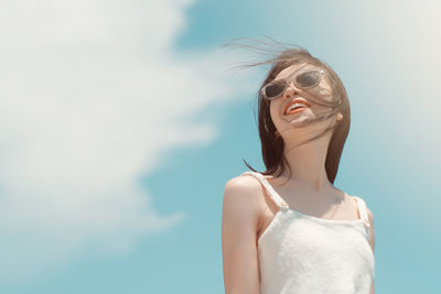 Low angle view of smiling young woman wearing sunglasses while standing against sky