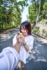 Cropped man giving flowers to girlfriend standing on road in forest