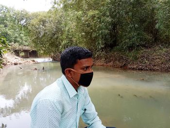 Close-up of young man wearing mask sitting by pond
