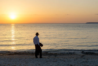 Rear view of silhouette man standing at beach during sunset