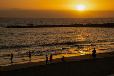 Silhouette people on beach against sky during sunset