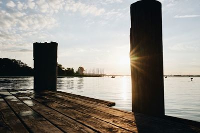 Wooden posts in lake against sky during sunset