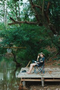Portrait of woman sitting by tree against plants
