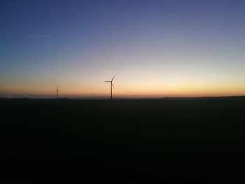 Silhouette wind turbines on field against sky during sunset