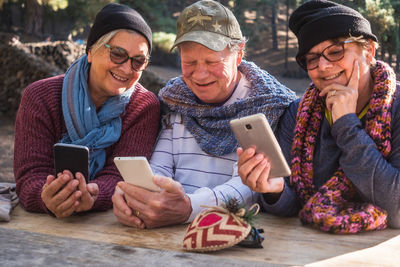 Senior friends using phones at table in forest
