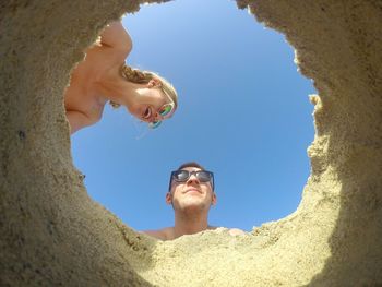 Shirtless man and woman seen through sand against sky