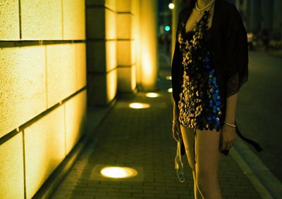 Midsection of woman standing on illuminated sidewalk at night