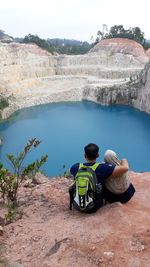 Rear view of couple looking at lake while sitting on mountain