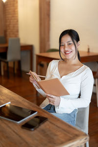 Portrait of smiling young woman using digital tablet while sitting on table