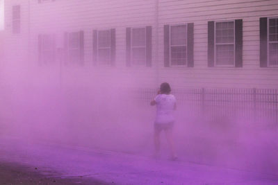 Rear view of woman walking on street surrounded by pink powder paint