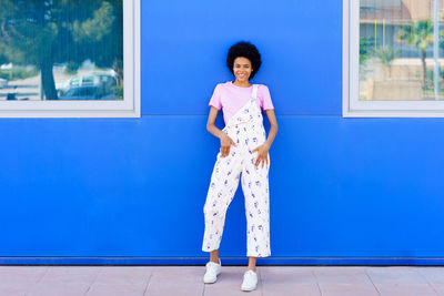 Portrait of young woman standing against blue wall