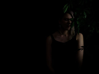 Portrait of young woman standing against black background