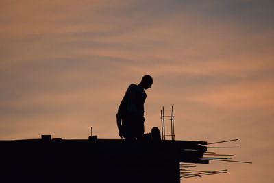 Silhouette worker standing on building against cloudy sky during sunset