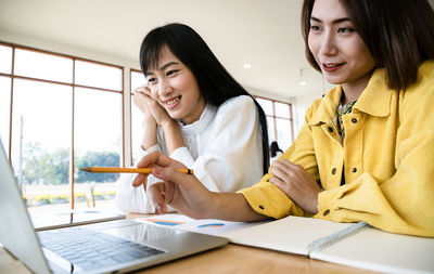 Young woman using phone while sitting on table