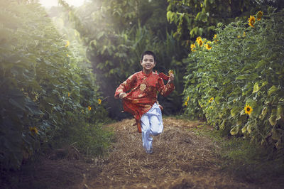 Portrait of smiling boy in traditional clothing running amidst plants