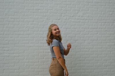 Full length of smiling young woman standing against brick wall