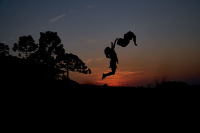 Silhouette man jumping on tree against sky