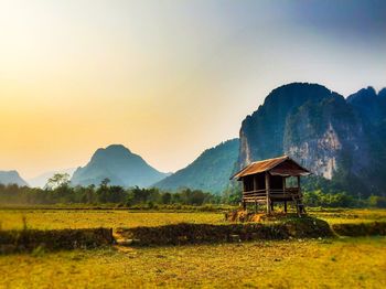 Barn on field by mountains against sky during sunset