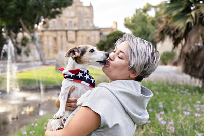 Woman holding and kiss on lips by small senior dog in park. joy, companionship between woman and dog