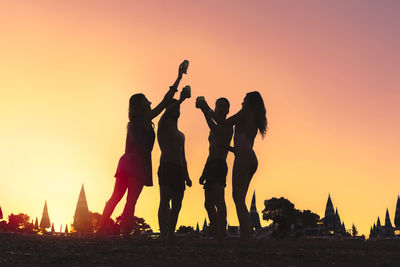 Silhouette people standing on the beach tossing with canned beers against sky during sunset