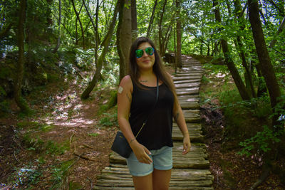 Portrait of smiling young woman standing amidst trees in forest