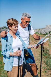 Senior couple with poles trekking looking map