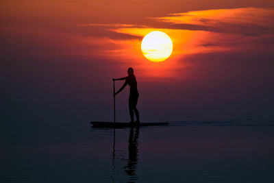Silhouette man standing in sea against sky during sunset