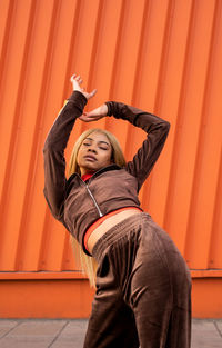 Cheerful african american woman in sportswear dancing in the street on an orange background