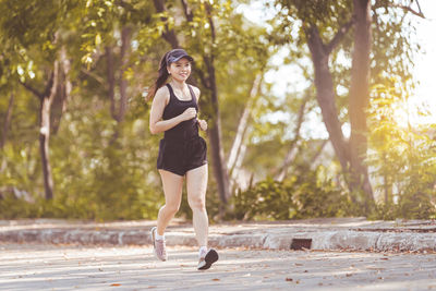 Full length portrait of a smiling young woman on footpath