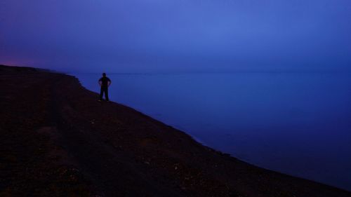 Silhouette man standing on shore against sky