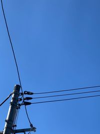 Low angle view of electricity pylon against clear blue sky