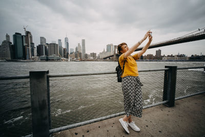 Woman taking selfie while standing against river in city