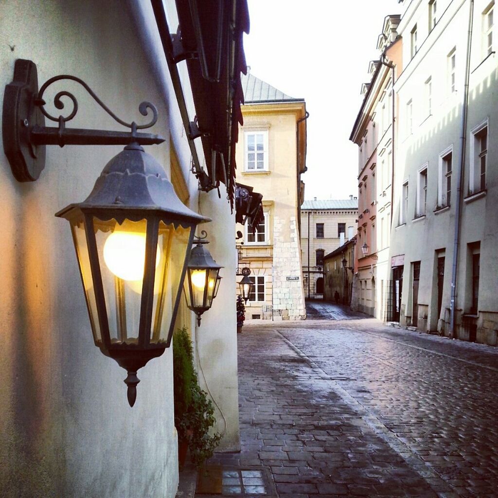 architecture, built structure, building exterior, lighting equipment, street light, the way forward, illuminated, street, building, residential building, residential structure, cobblestone, city, diminishing perspective, house, sunlight, no people, electric light, narrow, wall - building feature