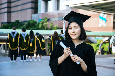 Young woman wearing black graduation gown standing in city