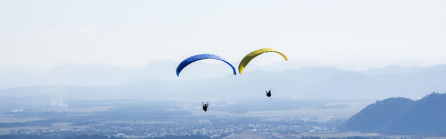 Panoramic view of people paragliding over landscape against sky