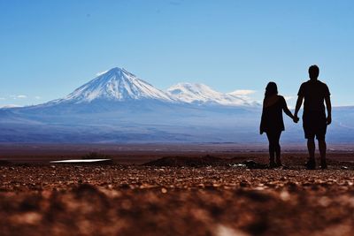 Rear view of silhouette couple holding hands while standing on field against clear blue sky