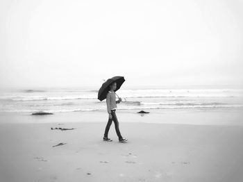 Girl walking on shore with umbrella at beach against clear sky