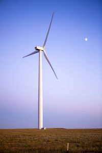 Wind turbines in field against blue sky at dusk with moon