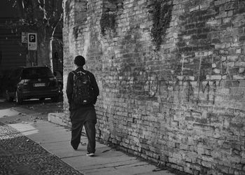 Rear view of man standing on footpath against wall