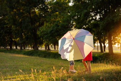 Low section of sibling holding umbrella standing at park