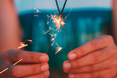 Midsection of person holding illuminated sparkler at night