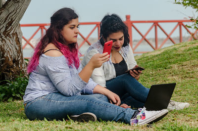 Full length of friends using technology at park