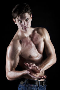 Portrait of young muscular man against black background