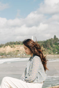 Side view of woman sitting against sky during sunny day